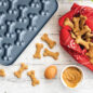 Baked dog treats in bone shapes on surface with blue Puppy Love Treat Pan next to treats