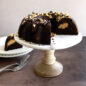 Chocolate Bundt® Cake with chocolate frosting, sprinkled with nuts and chocolate shavings, piece cut out