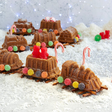 Baked train cake decorated in assortment of candies, formed in a train line on a pretzel track.