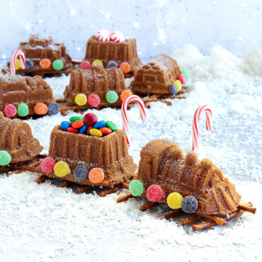 Baked train cake decorated in assortment of candies, formed in a train line on a pretzel track.