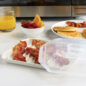 Compact Bacon Tray with Lid with bacon and plated pancakes, bowl of fruit, and glass of orange juice in front of microwave