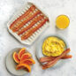 Overhead of Bacon Tray with bacon strips, plate of orange slices, plate of Scrambled Eggs and Bacon, and glass of orange juice