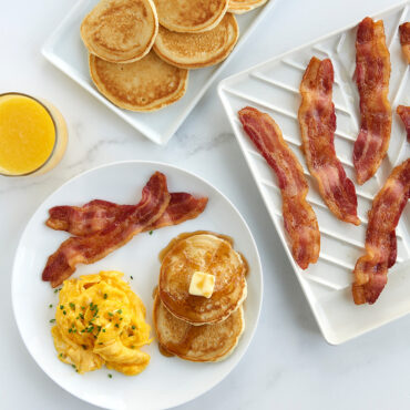 Overhead Large Slanted Bacon Tray with plate of pancakes, plate of bacon pancakes and eggs, and glass of orange juice