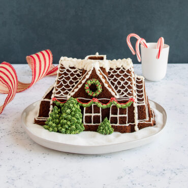 Decorated Gingerbread House Bundt® cake on a plate with candy canes  and decorative ribbon
