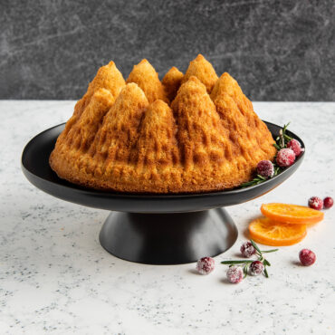 Pine Forest Bundt® cake on stand, plain with an orange slice and some berries