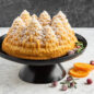 Pine Forest Bundt® cake on stand, covered in powdered sugar, with an orange slice and some berries