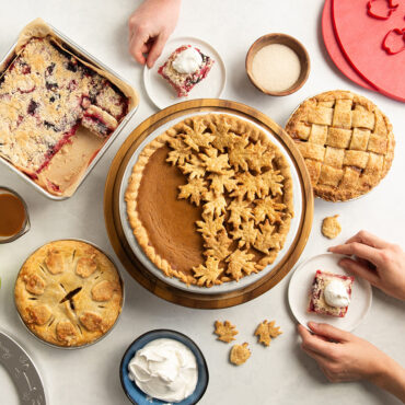 Group pie scene with 9" pumpkin pie in the center, two mini apple pies and pie bars in square baking pan.