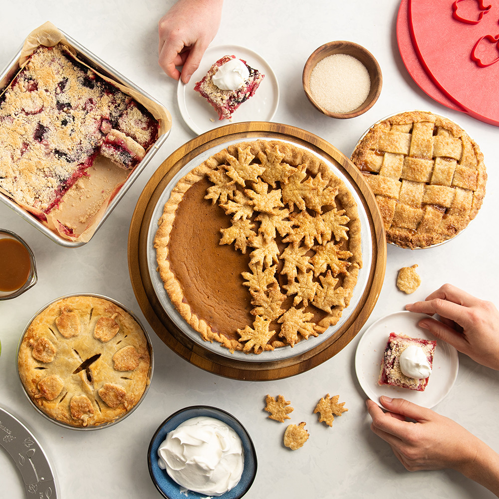 Image of group of baked pies lifestyle scene with hands grabbing plates with pieces of pie