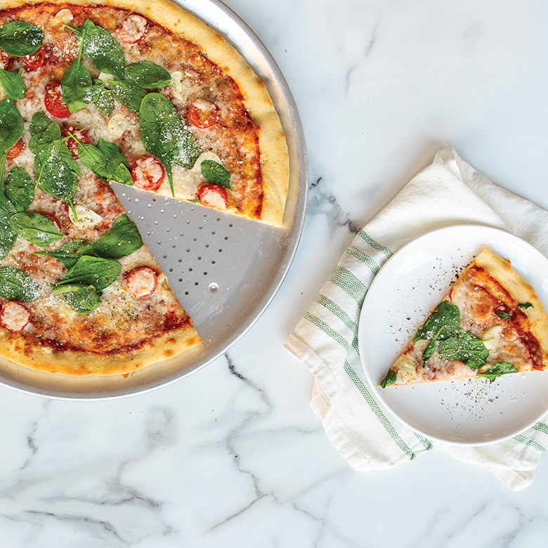 A Margherita pizza cooked on a Naturals 16 inch Hot Air Crisper Pan. Once slice is removed and served on a white plate next to the full pizza.