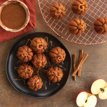 Lil' Pumpkin Cakelets on plate with caramel drizzle, with copper round cooling grid, apples and cinnamon sticks