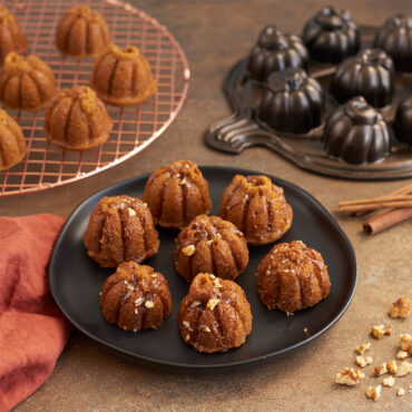 Lil' Pumpkin Cakelets on plate with caramel drizzle and nuts, with copper round cooling grid, pan, and cinnamon sticks