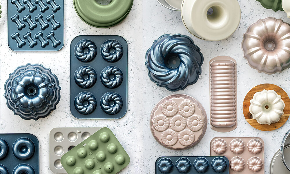 An overhead image of the Northern Lights Bakeware Collection featuring all of the different colors and styles offered in the line. This includes new swirl Bundt pans, formed aluminum Bundt pans, donut pans, specialty bakeware, and dog pans in all four new Northern Lights colors: Twilight Blue, Aurora Green, Golden Hour, and Glacier White. 