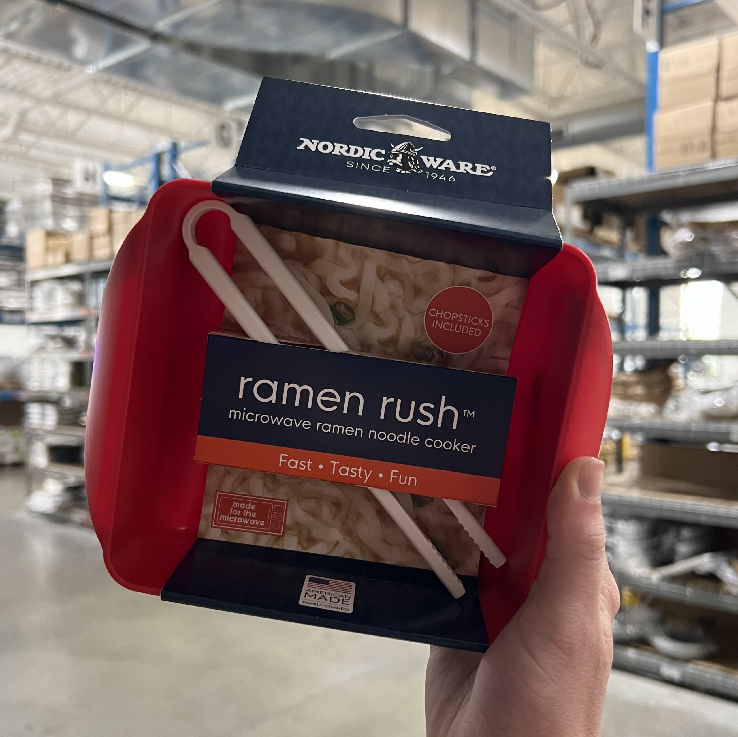 The Ramen Rush with Chopsticks in its full packaging held in a hand in front of the fulfillment center in the Nordic Ware factory. 