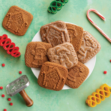 Gingerbread Cookies on plate against green background, surrounded by an assortment of holiday themed candies.