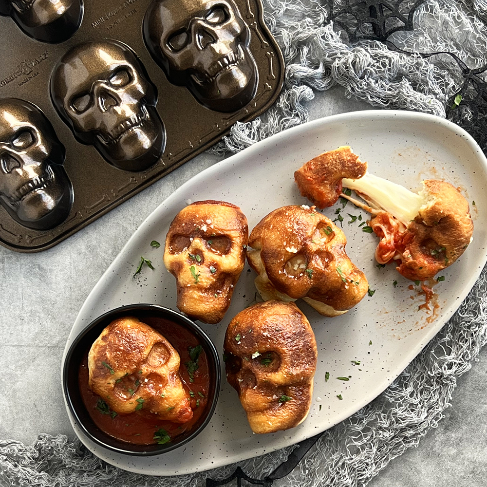 Overhead image of baked garlic bread skulls on a plate with pan next to it.