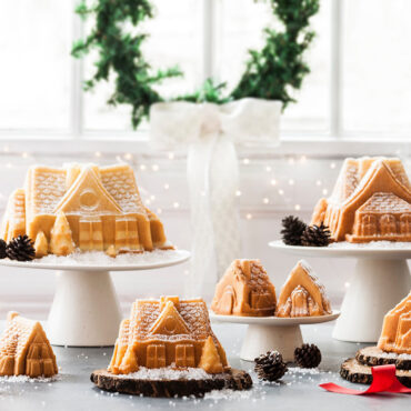 Baked vanilla full sized house cakes on cake stands, mini houses on cake stands, powdered sugar dusted, pine cone decorations