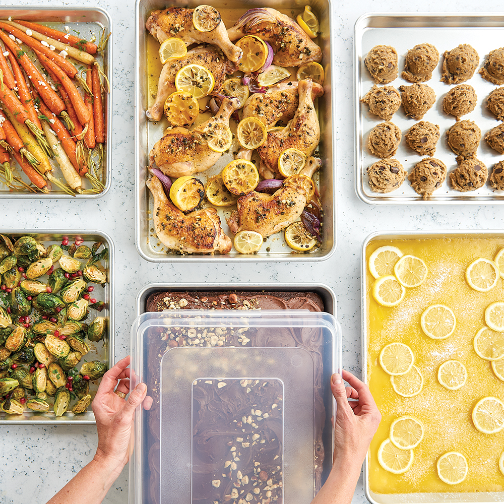 Image of sheet pans with different foods and hand putting lid on one sheet pan.