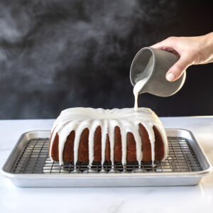  A fluted loaf cake on top of a Naturals® Quarter Sheet with Oven-Safe Nonstick Grid being glazed with vanilla glaze.