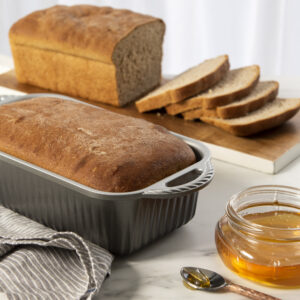 ProCast Classic Loaf Pan with bread baked in it next to an already sliced loaf on a cutting board and a jar of honey. 