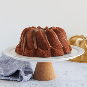 Brown Sugar Bundt Cake with Caramel Glaze made in the Nordic Ware Pirouette Bundt® Pan sitting on top of a white cake stand with the Pirouette Bundt® Pan in the background. 