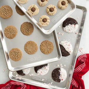 Naturals® Baking Sheet Set with Christmas cookies on them including peanut butter blossoms, shortbread cookies with starry night cookie stamp designs, and chocolate cookies dipped in white chocolate and peppermint. All of the pans are stacked on top of one another.