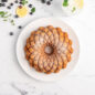 Powder sugar coated Kaleidoscope Bundt Cake on white plate, blueberries and lemon slice with glass of lemonade