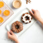 Classic Bundt Duet Cakes on plate being held, with bowl of cinnamon and cooling rack with orange slices