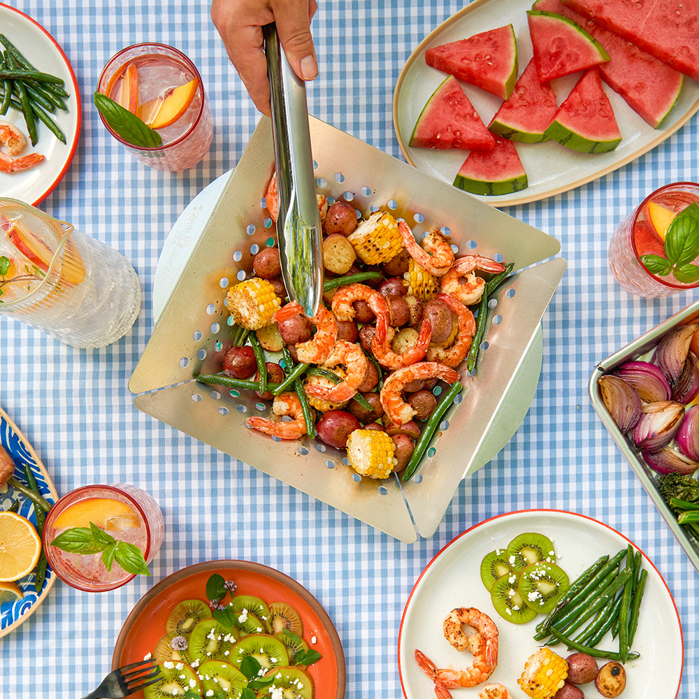 Overhead image of picnic table scene with grilling basket in center and food on platters